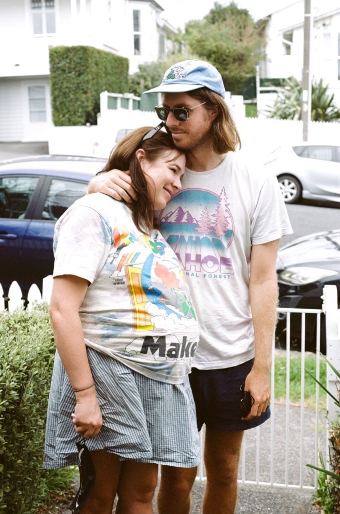Emily, left, is heavily pregnant and wears a graphic tee while Tom, right, hugs her in a front yard in this film photo. 