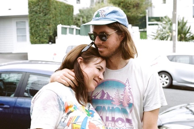 Emily, left, is heavily pregnant and wears a graphic tee while Tom, right, hugs her in a front yard in this film photo. 