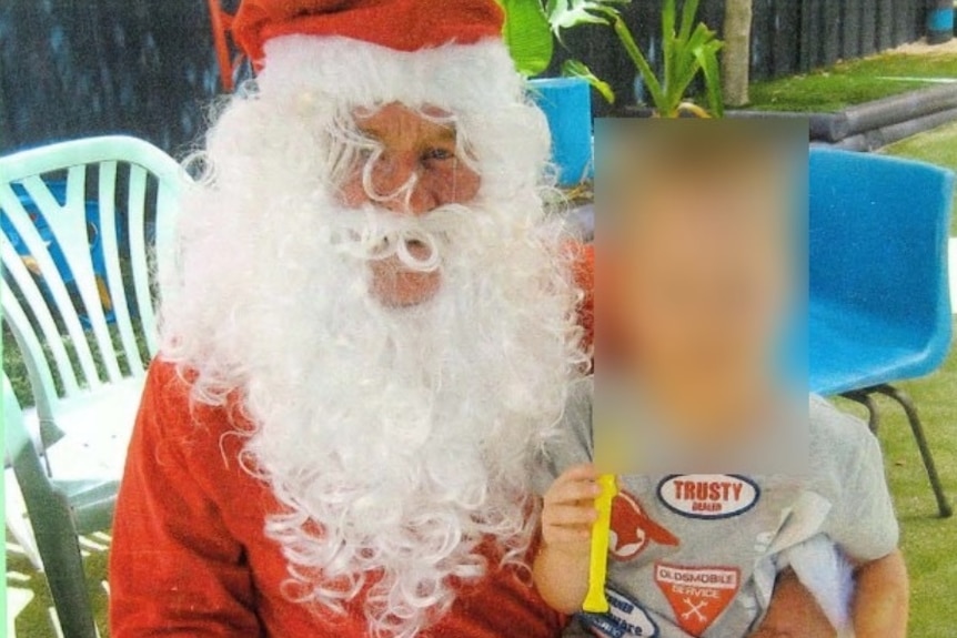A man dressed in a Santa suit poses with a child sitting on his knee