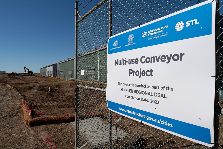 A sign on a wire fence with construction behind, reading 'multi-use conveyor project' 