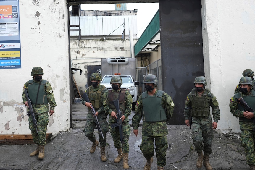 Soldiers walk out of a gate wearing riot gear and carrying guns. 