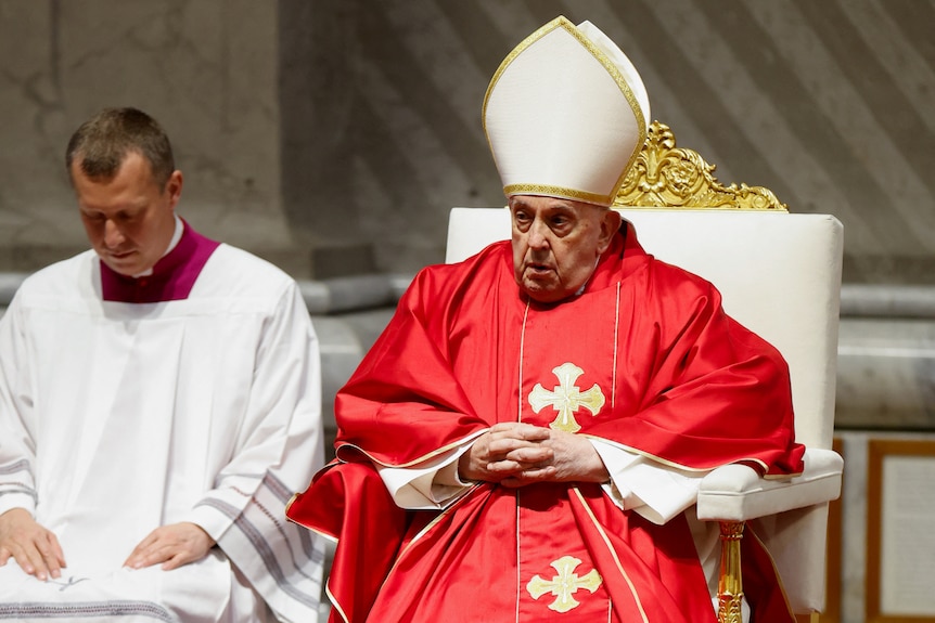 The pope - an old white man - wearing a red robe and white hat in church.