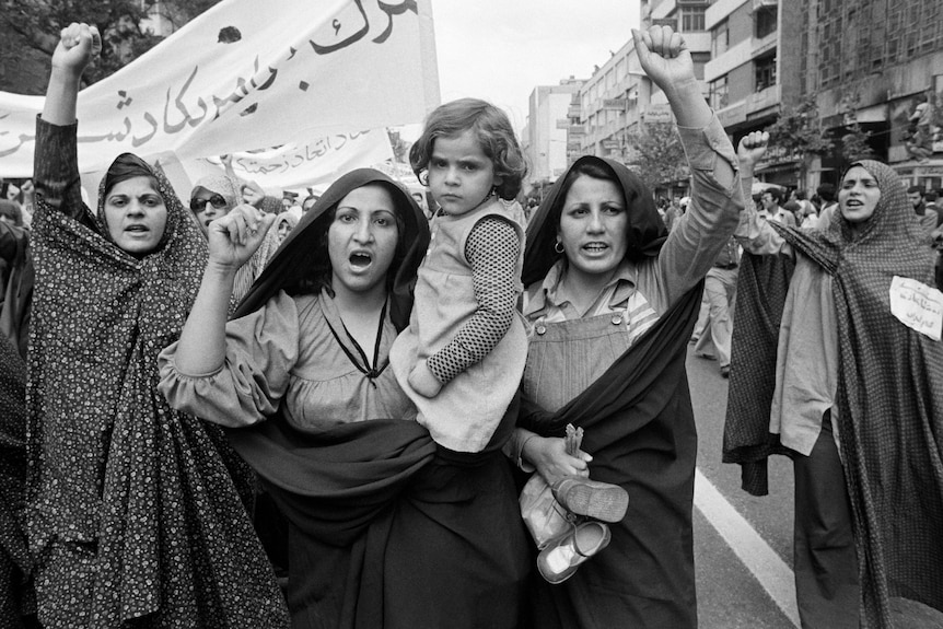 A black and white photo of women in Islamic veils protesting, one holding a child.