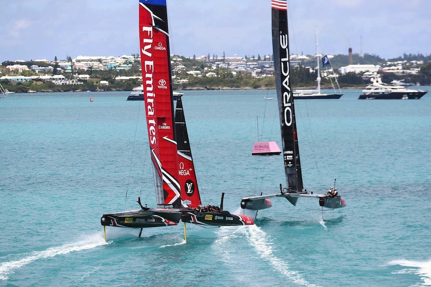 Two sailboats sail close together in Bermuda waters near the coastline with other boats in the distance