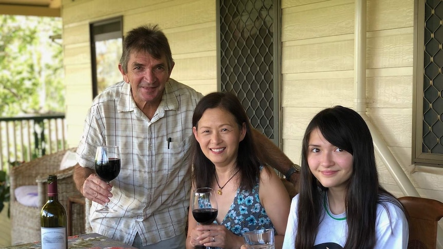 Wayne and Jemma Binney hold glasses of wine in front of a cheese platter with their daughter.