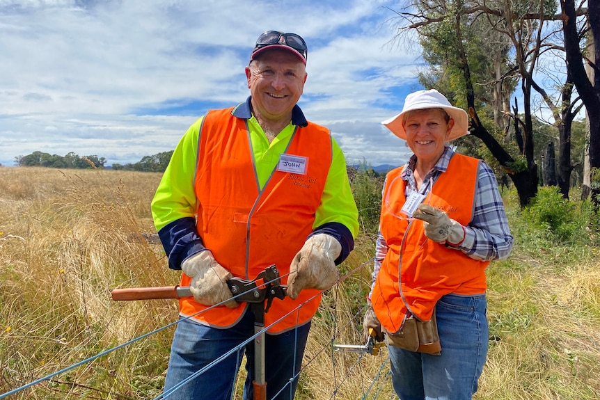  A man and a woman smiling and holding fencing equipment on a fence line. 