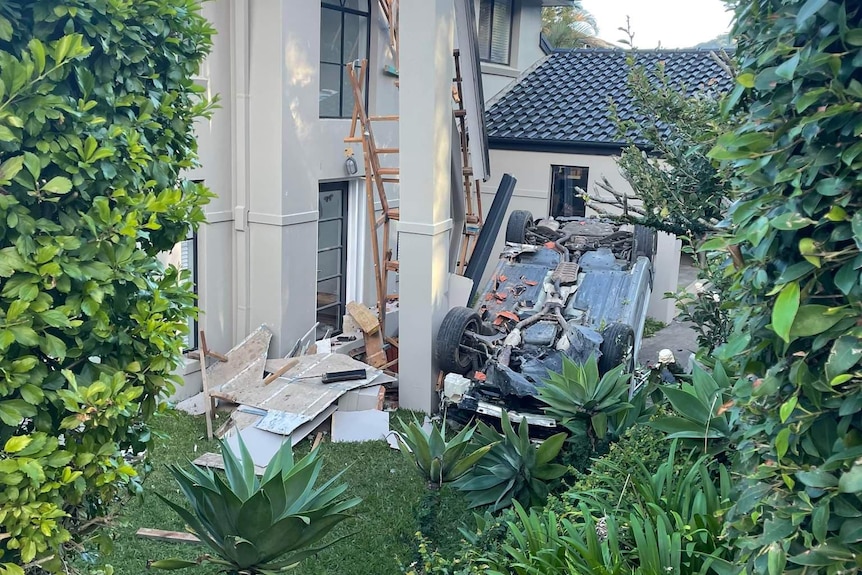 Car upside down in a front yard of a large home