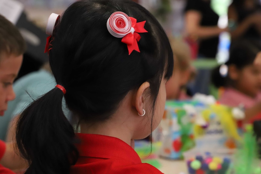 An unidentifiable girl with a red hair clip in a classroom.