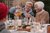 Picture of a woman pouring her mother a glass of drink in an outdoor feast