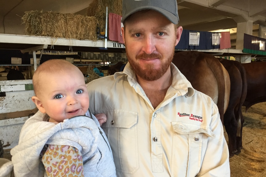 Man holding a baby in the cattle sheds at The Ekka.