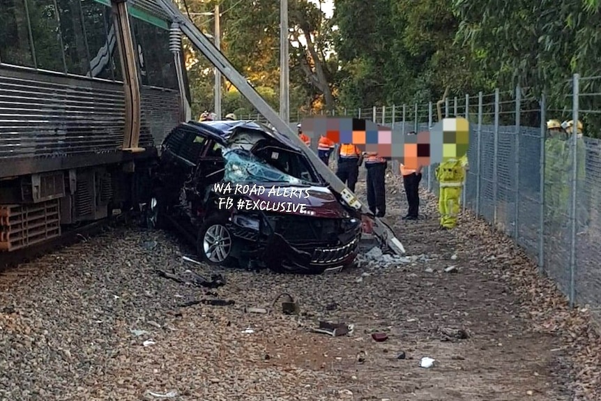 A badly damaged car next to a train.