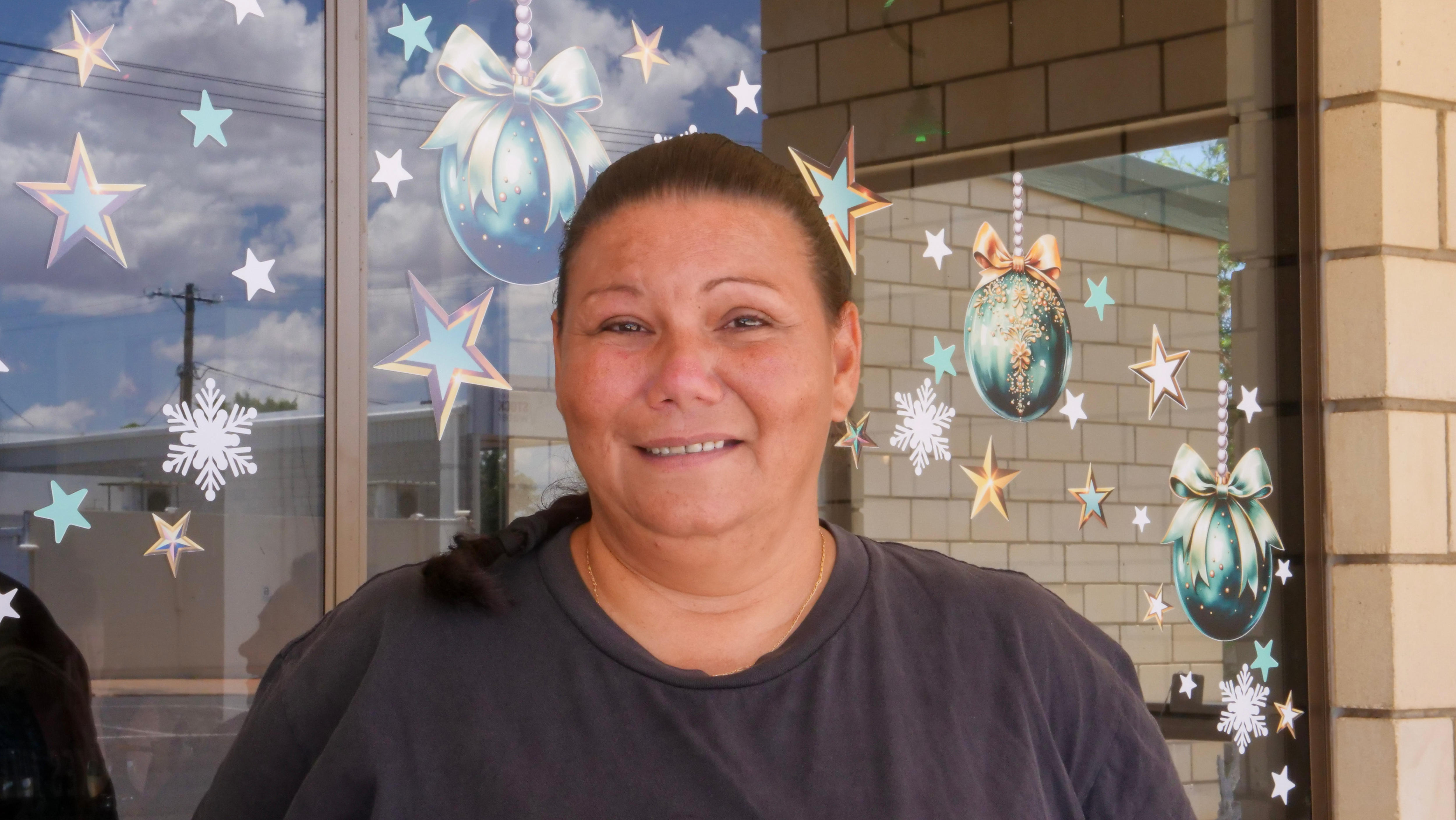 Uma mulher sorri para a câmera em frente à janela de um pub coberta de decorações de Natal.