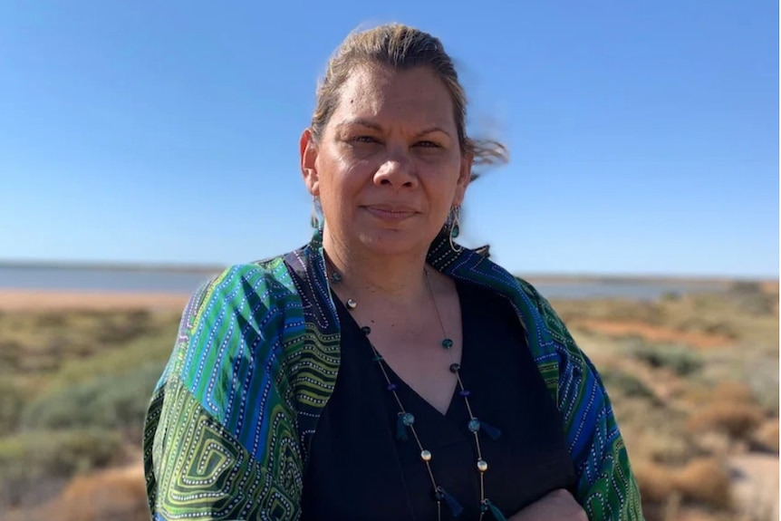 A close of a woman with scrub in the background.