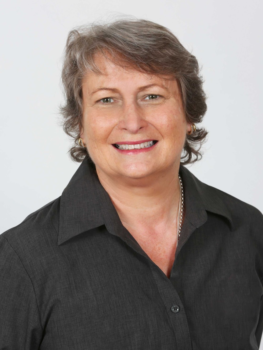 A middle-aged woman with short grey hair and a black shirt smiles at the camera.