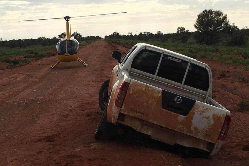 A car is stuck in the muddy road while a chopper lands in the background