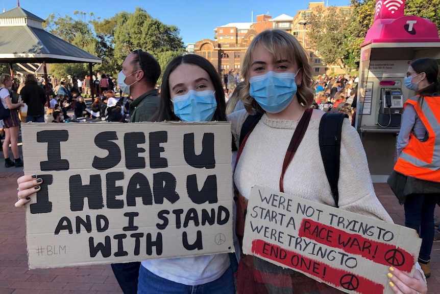 Two girls in face masks holding signs