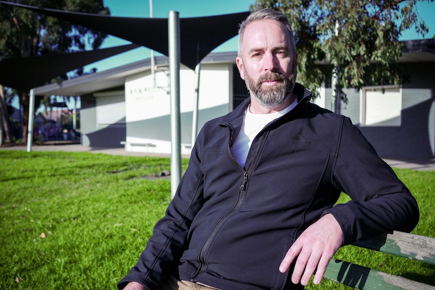 David Berry who runs a debt support service sitting on a park bench in a navy zip up fleece.