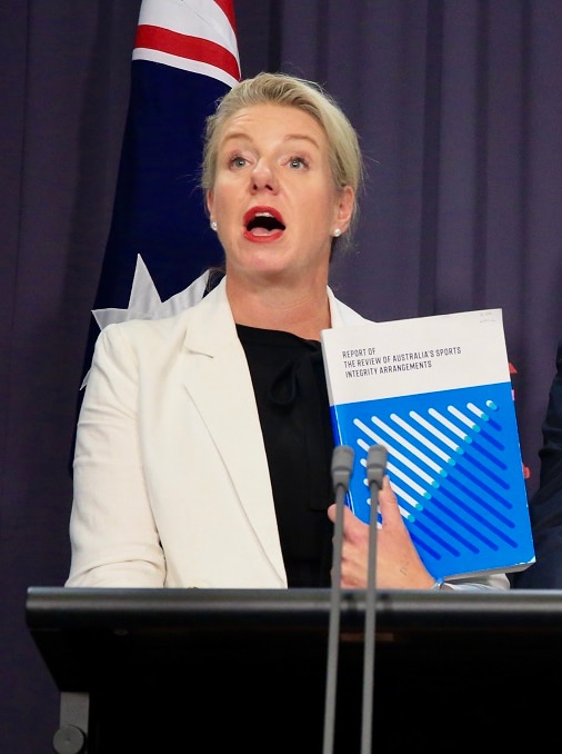 A politician holds a report up as she speaks from behind a lectern at a media conference