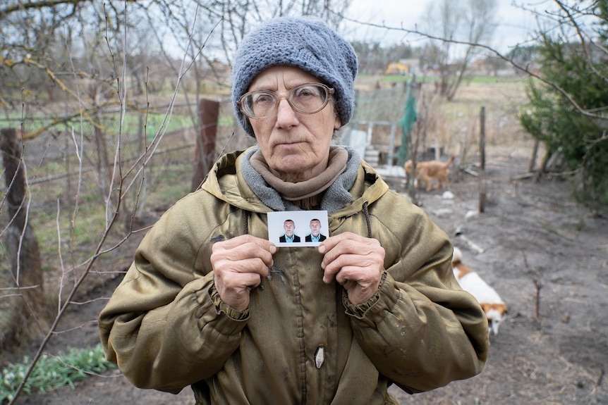 A woman holds up two small passport photos of a young Ukrainian man.