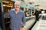 Geoff Hutchison leaning out of a train's open door at the train station platform.