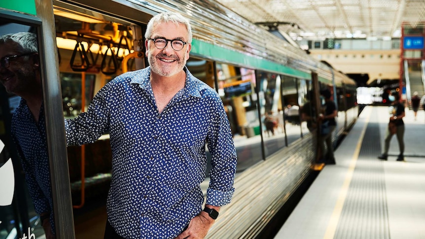 Geoff Hutchison leaning out of a train's open door at the train station platform.