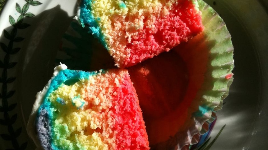A cupcake in rainbow colours, split open down the middle.