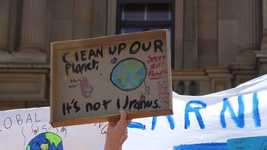 A hand holding up a sign saying: "Clean up our planet, it's not Uranus."