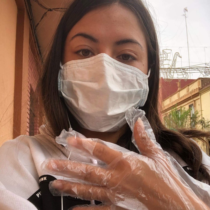 A woman in a face masks shows off a disposable glove