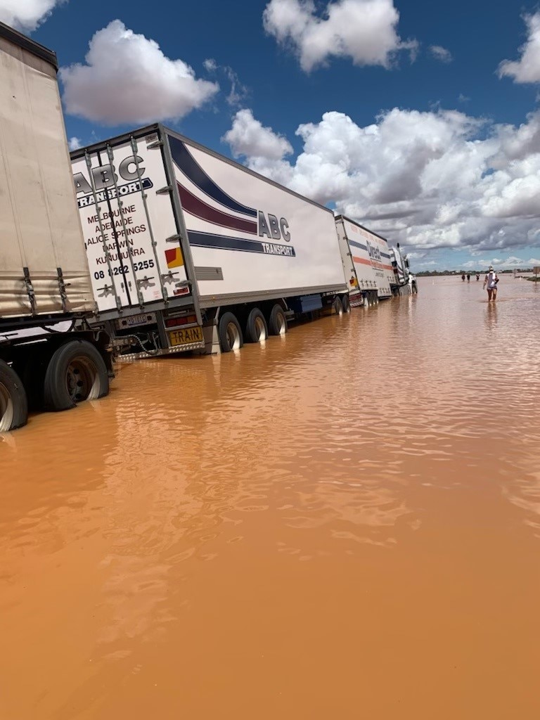 Road train leaning to left side in murky brown water.