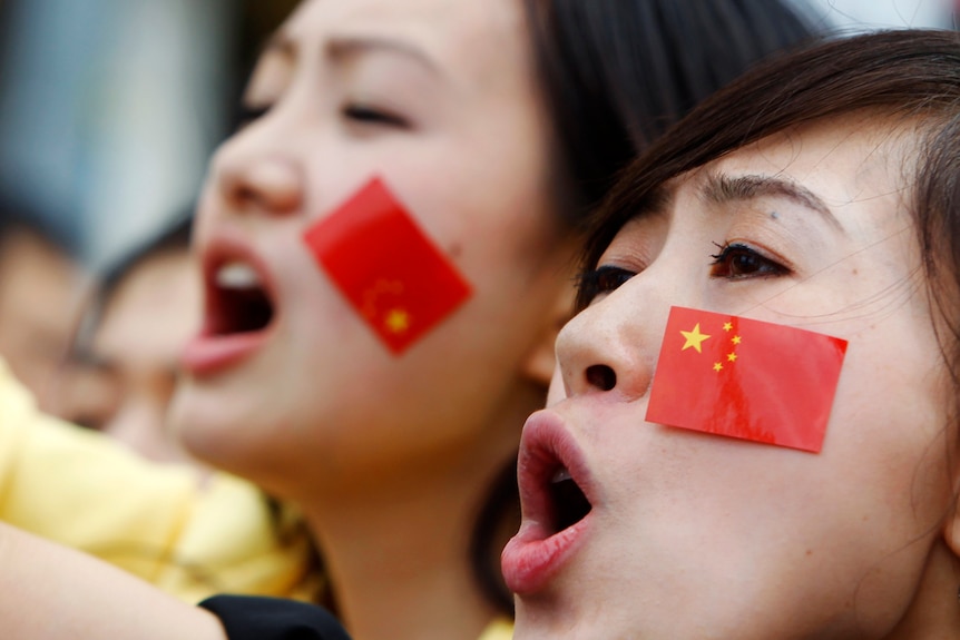 Two women with mini Chinese flags stuck to their cheeks