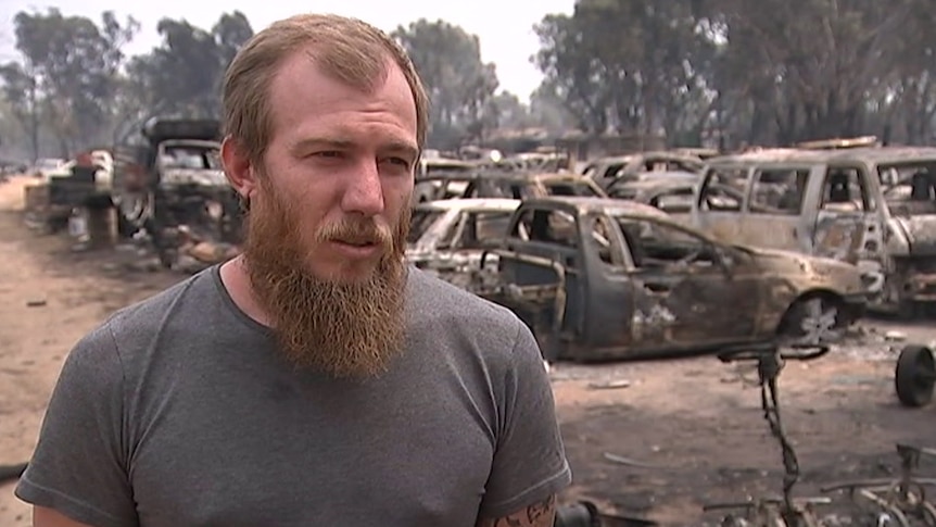 A man stands in front of burnt out cars