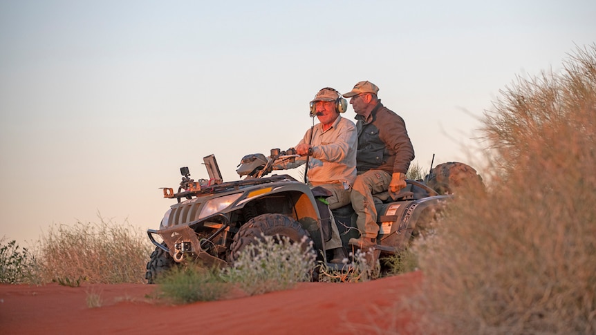 Two men riding on a quad bike through the Simpson Desert at sunset