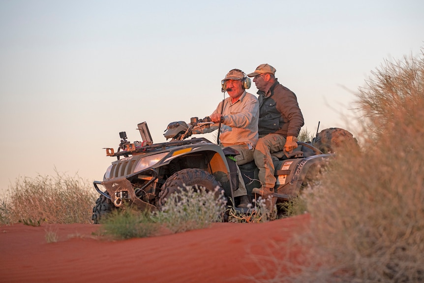 Two men riding on a quad bike through the Simpson Desert at sunset