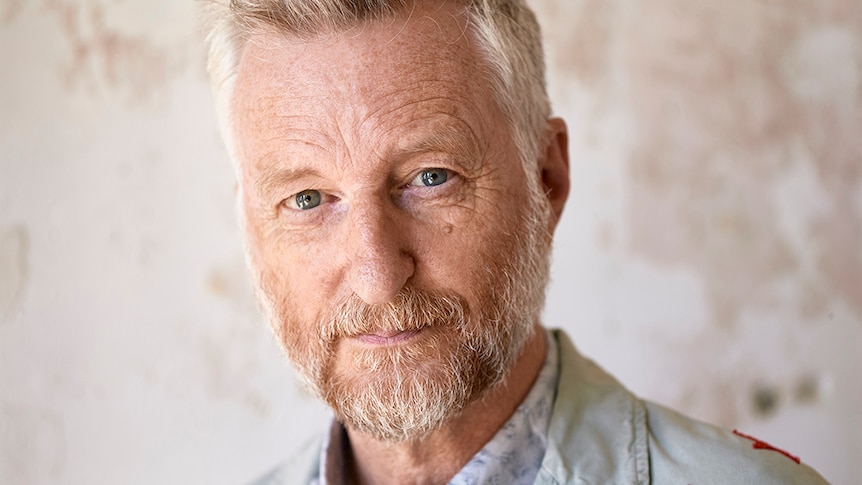 Billy Bragg stares into the camera, wearing a light blue jacket