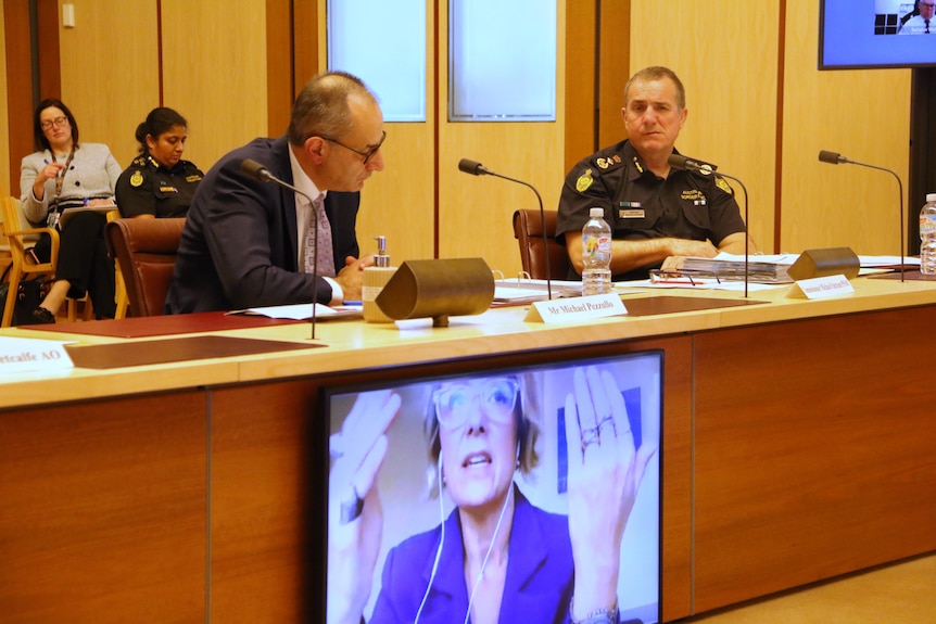 Kristina Keneally, displayed on a screen, questions Mike Pezzullo and Michael Outram.
