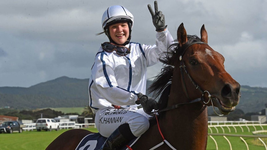 A young female jockey smiling on top of a racehorse.