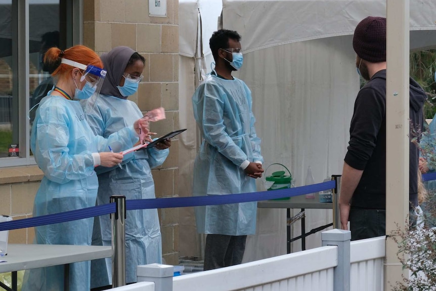 Two women and a man in PPE attend a coronavirus testing station.