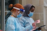 Two women and a man in PPE attend a coronavirus testing station.