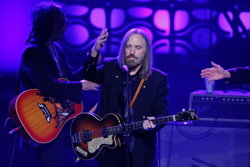 Musician Tom Petty holding a guitar performs on stage.