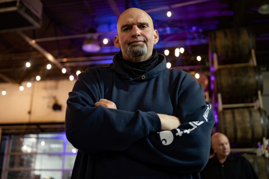 A bald man in a hoodie folds his arms across his chest 