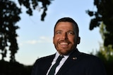 A man sitting in a wheelchair who has short hair and is wearing a black suit