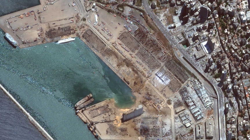 A large crater is visible at the site of the explosion in the port.