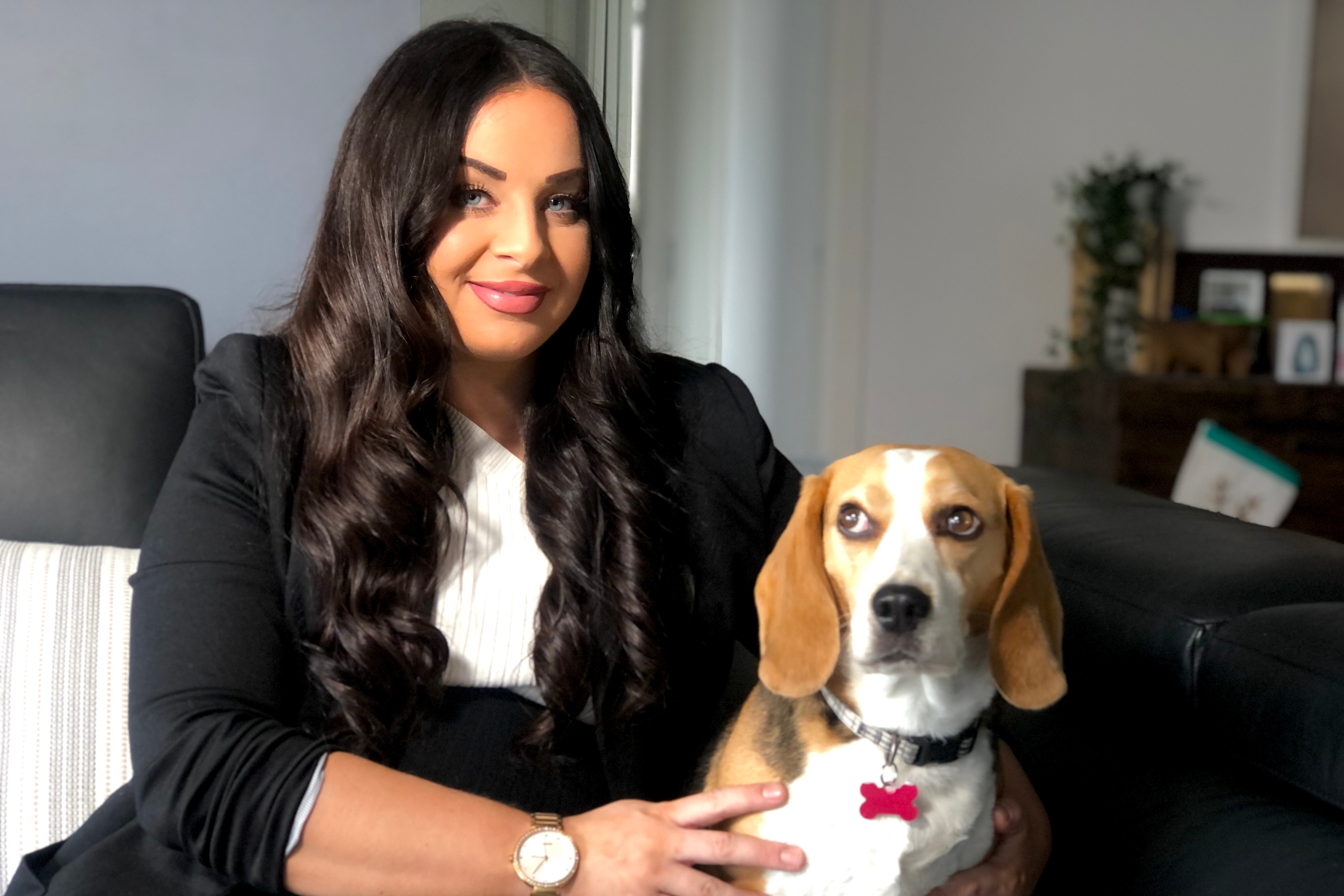 A young white woman with long dark hair sitting on a couch with a beagle
