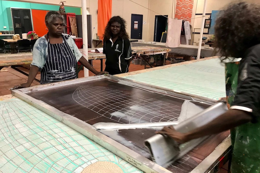 Three Aboriginal women using a screen print frame to print an image on fabric.