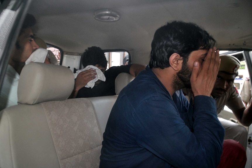 Three Indian men accused of gang-raping a woman are taken to court in a car.