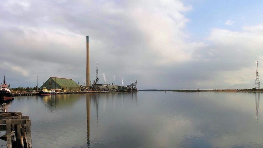 A large smoke stack and buildings stand behind a larger river.