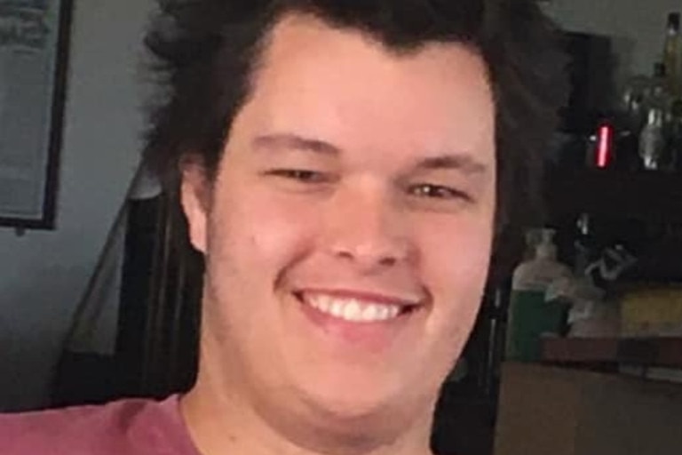 A man with pointy hair and maroon t-shirt smiling at the camera