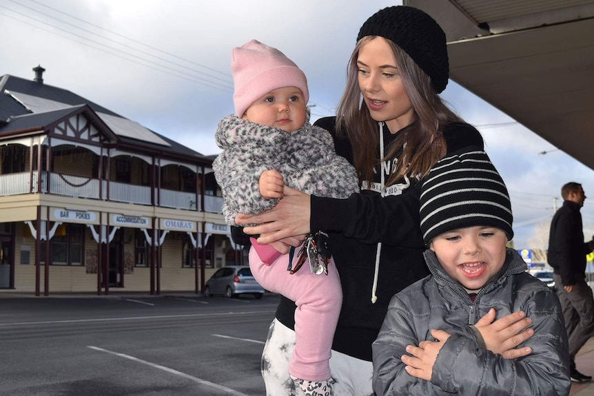 A woman holding a baby and a young boy, all rugged up in beanies for cold weather