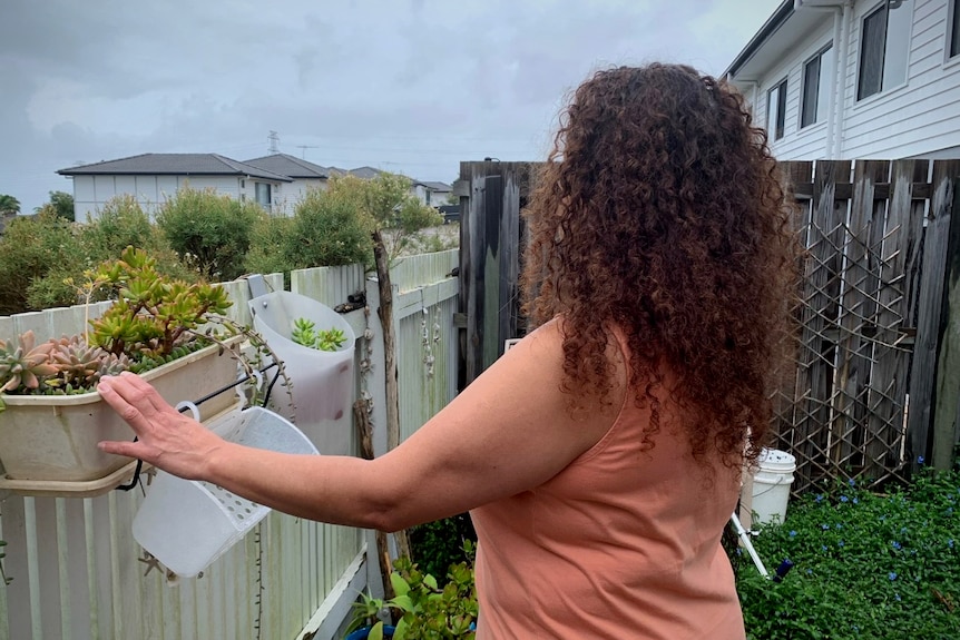 a woman, her face obscured, standing in her back garden next to the fence line