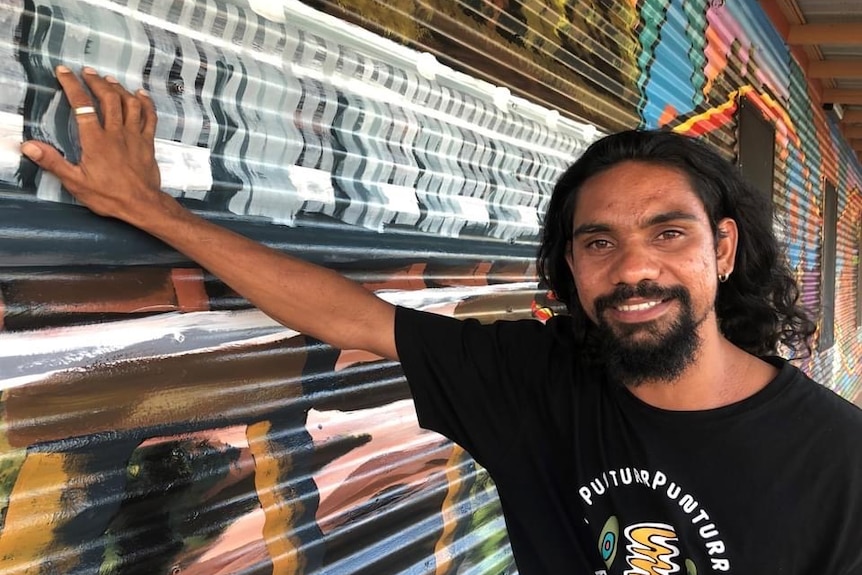 A young Indigenous man leaning against a wall.